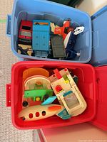 Red storage bin containing additional Fisher-Price vehicles and playset components including airplane fuselage