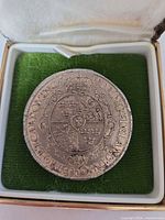 Front view of coin in box displaying reverse crowned shield