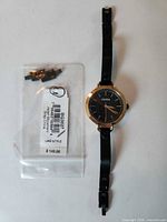 Watch with bracelet fully extended beside bag of spare links and label