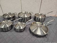 Five stainless steel pots and pans with lids displayed together