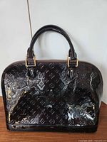 Front view of Louis Vuitton deep burgundy patent leather handbag showing monogram pattern, shape and handles