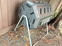 Compost tumbler on stand beside fence