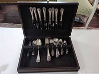 Flatware set displayed in open wood chest showing assorted utensils