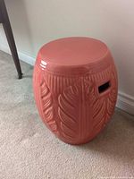 Front view of coral ceramic garden stool showing leaf relief and handle