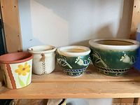 Four planters on shelf: multicolor floral terracotta, white speckled ceramic, two green hand-painted floral ceramic