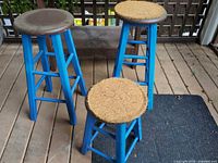 Three stools showing two tall and one low, blue legs, round seats