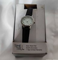 Watch in retail display showing dial, strap, and packaging text