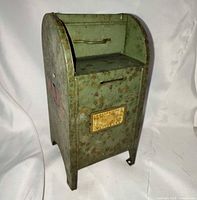 Front angled view of metal mailbox bank showing overall form, coin slot and plaque