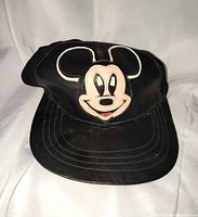 Front view of black leather cap showing Mickey Mouse applique and brim