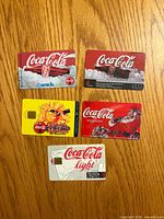 Front view of five Coca-Cola themed phone cards on wood surface