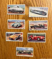 Fronts of seven illustrated British racing car cards displayed on wood surface