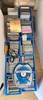 Top view of stacked blue crates holding numerous CDs and DVDs with boombox cable visible