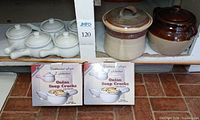 Shelf view showing five white crocks, two boxed sets of crocks, and two stoneware bean pots