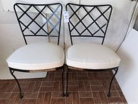 Front view of both black metal lattice-back chairs with white cushions
