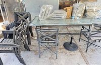 Glass-top table, multiple metal chairs, umbrella base, packaged cushions visible