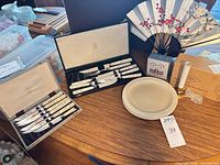 Overview of entire lot on tabletop showing cased flatware, plates, fans, shakers and candle set