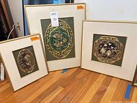 All three framed silk embroideries standing on floor