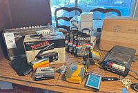 Group shot of all items on table including Grundig radio, Pollenex box, Sony Walkman, cassette recorder, sealed Maxell tapes, accessories
