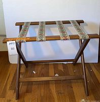 Front view of wood folding luggage rack showing floral tapestry straps and X-frame legs