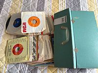 Open teal record case with stack of 45s in sleeves, RCA orange label record visible