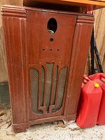 Front view of Art Deco wood radio console cabinet showing dial opening, control holes, speaker grille, and surface wear