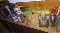 Full lot view showing assorted cups, mugs, tumblers, goblet, stacks of disposable cups and swizzle sticks