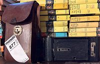 Camera closed beside leather case; spine view