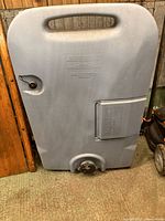 Front view of gray Tote-N-Stor portable waste water tank showing handle, fill cap, storage hatch and drain outlet