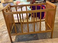 front view of wooden doll crib showing slatted sides and perforated base