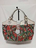 Front view of Guess floral denim handbag with faux snakeskin trim and logo buckle