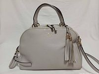 Front view of Kate Spade light gray satchel showing overall design, tassels, handles and logo