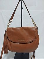 Front view of brown Michael Kors Bedford leather crossbody bag showing flap, logo, tassel, and strap