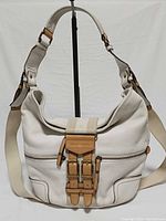 Front view of white leather satchel showing front zip pocket, canvas strap flap, buckles