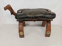 Full side view of camel saddle stool showing wood frame, leather seat, brass mounts