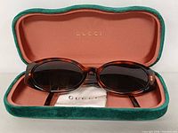Open green velvet case showing Gucci logo, sunglasses and cloth