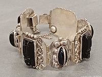 Full view of hinged silver bracelet showing carved onyx masks and cabochons