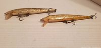 Two lures left side view showing gold scale finish, diving lips, treble hooks