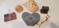 Group shot showing all six items: two seashells, grey heart plaque, flag plaque, dog figurine, metal Arc de Triomphe paperweight