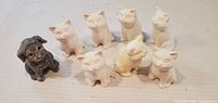 Front view of seven white bisque cats and one grey dog
