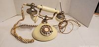 Full view of cream rotary telephone with handset on cradle and cords