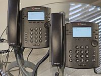 Front view of both Polycom VVX 311 phones with displays lit, handsets attached, coiled cords visible