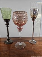 Front view of all three glass and metal candle holders showing varying colors, stems and heights