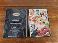 Front graphics of one tin and back of the other on wood table