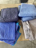 Four folded moving blankets on table, assorted blue shades
