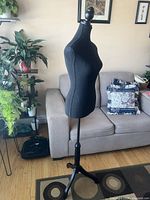 Full view of black fabric dress form on wooden tripod base