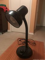 Side view of black gooseneck desk lamp showing shade, neck, cord and base