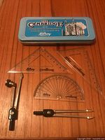 Full set displayed: tin, compasses, ruler, triangles, protractor