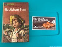 Front cover of Huck Finn book alongside Halloween gift certificate