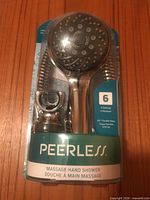 Front of packaged Peerless handheld shower showing showerhead, hose, holder