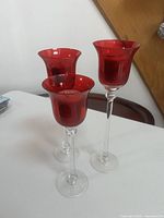 three red glass candle holders with clear stems standing on table